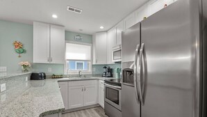 A modern kitchen with white cabinets, stainless steel appliances, granite countertops, and a window with a view.