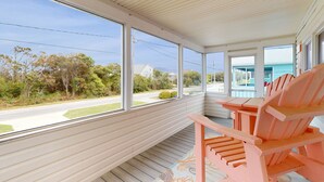 A covered porch with large windows, wooden flooring, and pink Adirondack chairs.