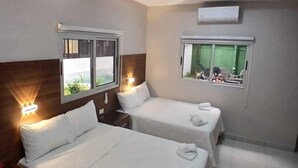 Een hotelkamer met twee bedden, een plafondventilator en ramen met gordijnen.