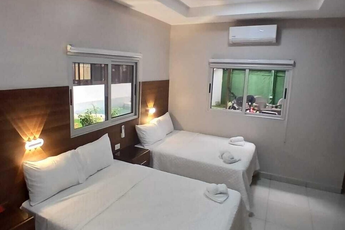 A hotel room with two beds, a ceiling fan, and windows with curtains.