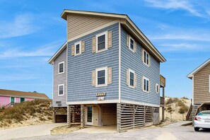 A two-story building with a garage, a visible address sign, and a sandy beach in the background. - Large 3BR Oceanfront | Deck | Tennis | W/D (Nags Head)