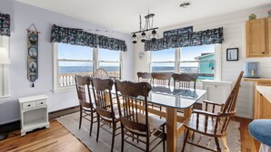 Un coin repas avec une table en verre et des chaises en bois, un buffet blanc et une vue sur l’océan.