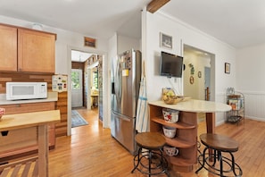 A kitchen with wooden cabinets, a stainless steel refrigerator, a microwave, a TV, and a wooden dining table with stools. - Tranquil 4BR Waterview | Fireplace | Deck (Southern Shores)