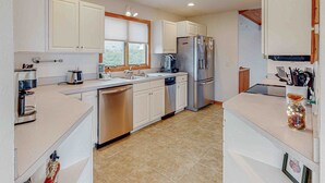 A modern kitchen with white cabinets, stainless steel appliances, and a tiled floor. - SH03: SS OBX | Sunny Home| Dog-Friendly | Private Pool (Southern Shores)