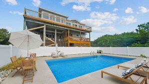 A swimming pool with lounge chairs and a table, surrounded by a white fence and a wooden deck. - SH03: SS OBX | Sunny Home| Dog-Friendly | Private Pool (Southern Shores)
