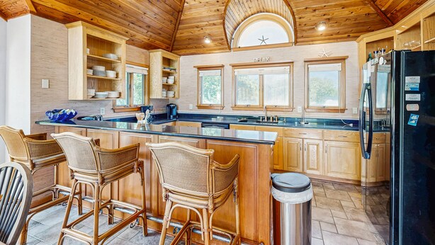 A spacious kitchen with wooden cabinets, a large island with bar stools, and a black refrigerator. - 4BR Dog Friendly | Private Pool | Hot Tub (Southern Shores)