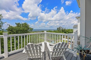 A deck with white railings, two Adirondack chairs, and a view of a house and greenery. - Waterfront home with private pool & hot tub - in-home elevator & pool table (Corolla)