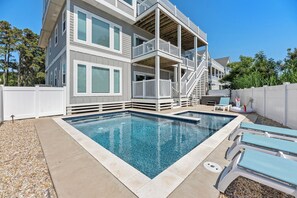 A two-story building with a swimming pool, outdoor seating, and a white fence.