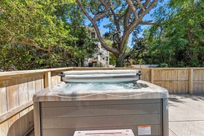 Un bain à remous entouré de clôtures en bois, avec des arbres et un bâtiment en arrière-plan.