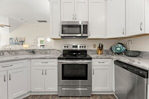 Una cocina moderna con armarios blancos, una estufa de acero inoxidable, un microondas y un lavavajillas.