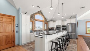 A spacious kitchen with a large island, white cabinetry, and a stone accent wall. - 10BR | Private Pool | Hot Tub | Elevator (Corolla)