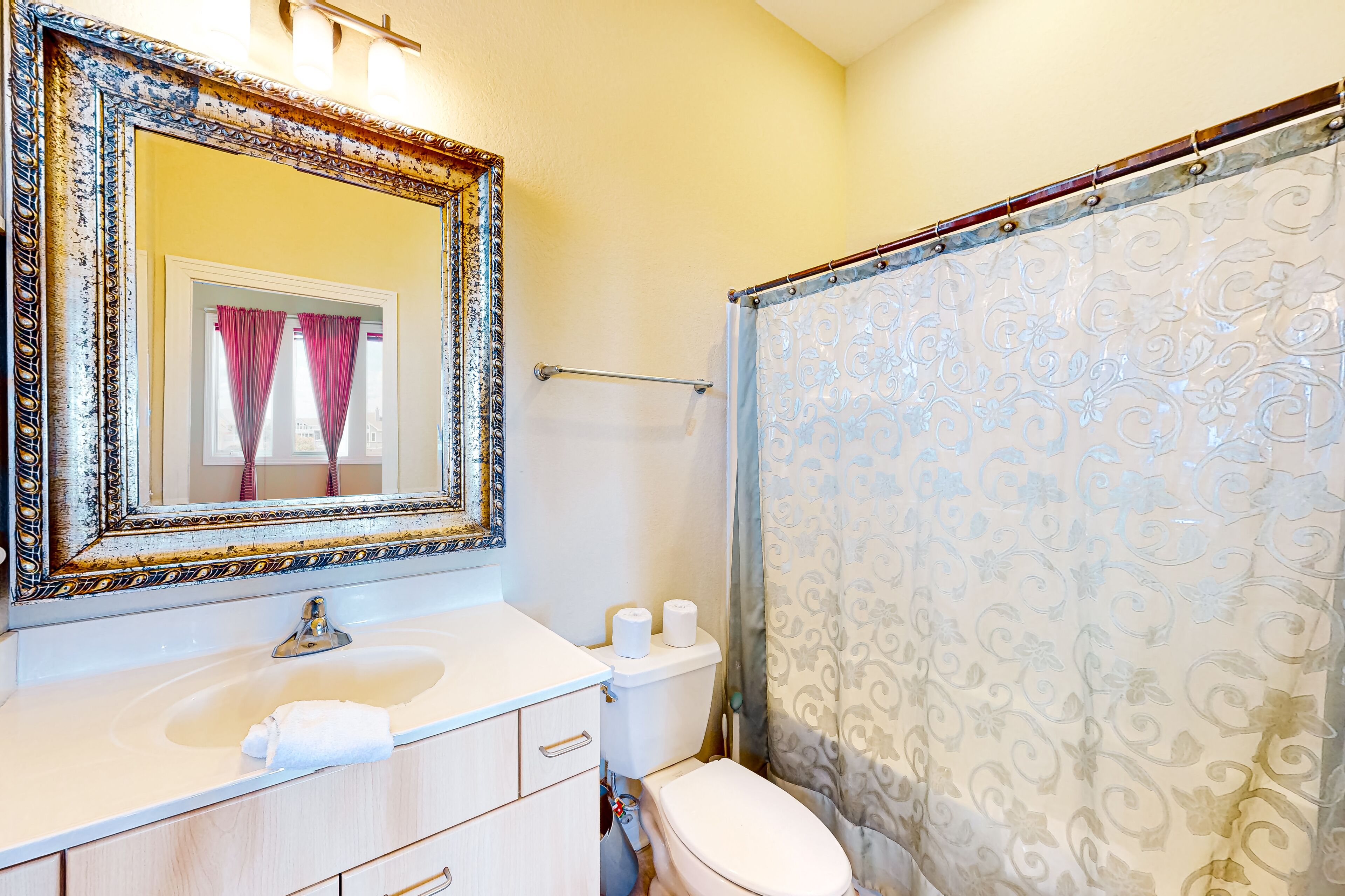 A bathroom with a large ornate mirror, a sink, a toilet, and a shower curtain with a floral pattern.