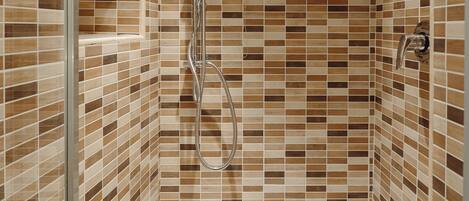 A shower with a glass door, tiled walls, and a handheld showerhead.
