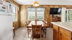 A dining area with a wooden table and chairs, a hanging light fixture, and a television on a stand.
