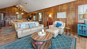 A spacious living room with a large sofa, a coffee table, and a dining area with wooden furniture.
