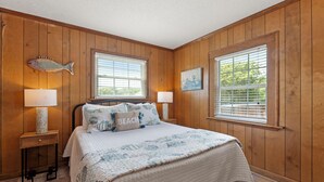 A bedroom with wooden walls, a bed with a quilt, two bedside lamps, and a fish decoration on the wall.
