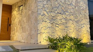 A modern building with a stone facade, a wooden door, and a well-lit entrance area with steps and plants.