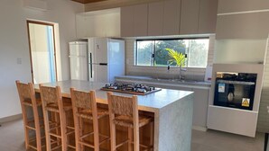 A modern kitchen with a central island, wooden bar stools, a gas stove, and a refrigerator.