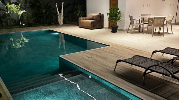 A modern outdoor pool area with a wooden deck, lounge chairs, and a dining set.