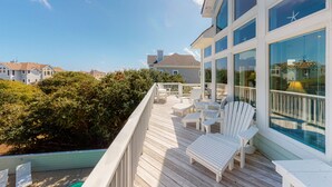 Terraza de madera con sillas blancas y una piscina, con vista a una zona residencial.