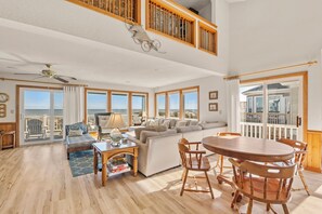 A spacious living room with a high ceiling, large windows, a balcony, and a dining area.