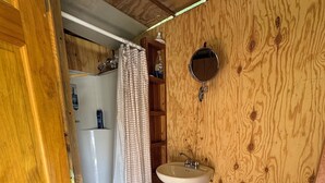 Un baño pequeño con pared de madera, un lavamanos blanco, un espejo y un calentador de agua.
