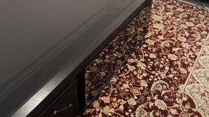 Un salon avec une table basse en bois foncé, deux canapés de couleur crème ornés de coussins à motifs, un tapis à motifs et un coin repas avec des chaises et une table en bois.