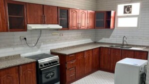 Une cuisine avec des meubles de rangement en bois, un four encastré, un évier et un réfrigérateur.