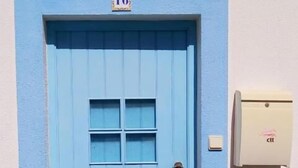 Eine blaue Tür mit einer Nummernschild '16' darüber, einem kleinen Fenster und einem Klingelknopf auf der rechten Seite.