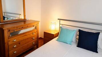 A bedroom with a bed, a wooden dresser with drawers, a bedside table, and a lamp.
