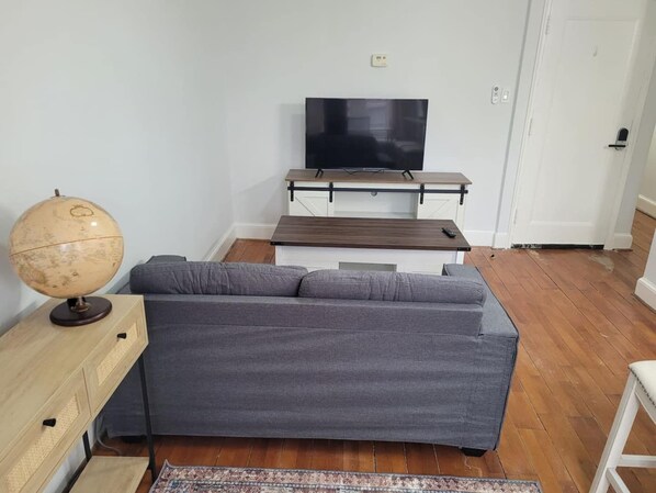 Een woonkamer met een grijze bank, een houten salontafel, een wereldbol en een flatscreen televisie op een standaard.