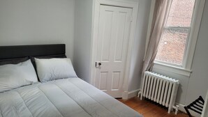 Un dormitorio con cama, puerta, ventana y radiador.