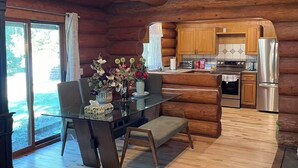 A spacious log cabin interior with a wooden dining table, chairs, and a kitchen area. - TreeHouse Nook Bed & Breakfast (Ladysmith)