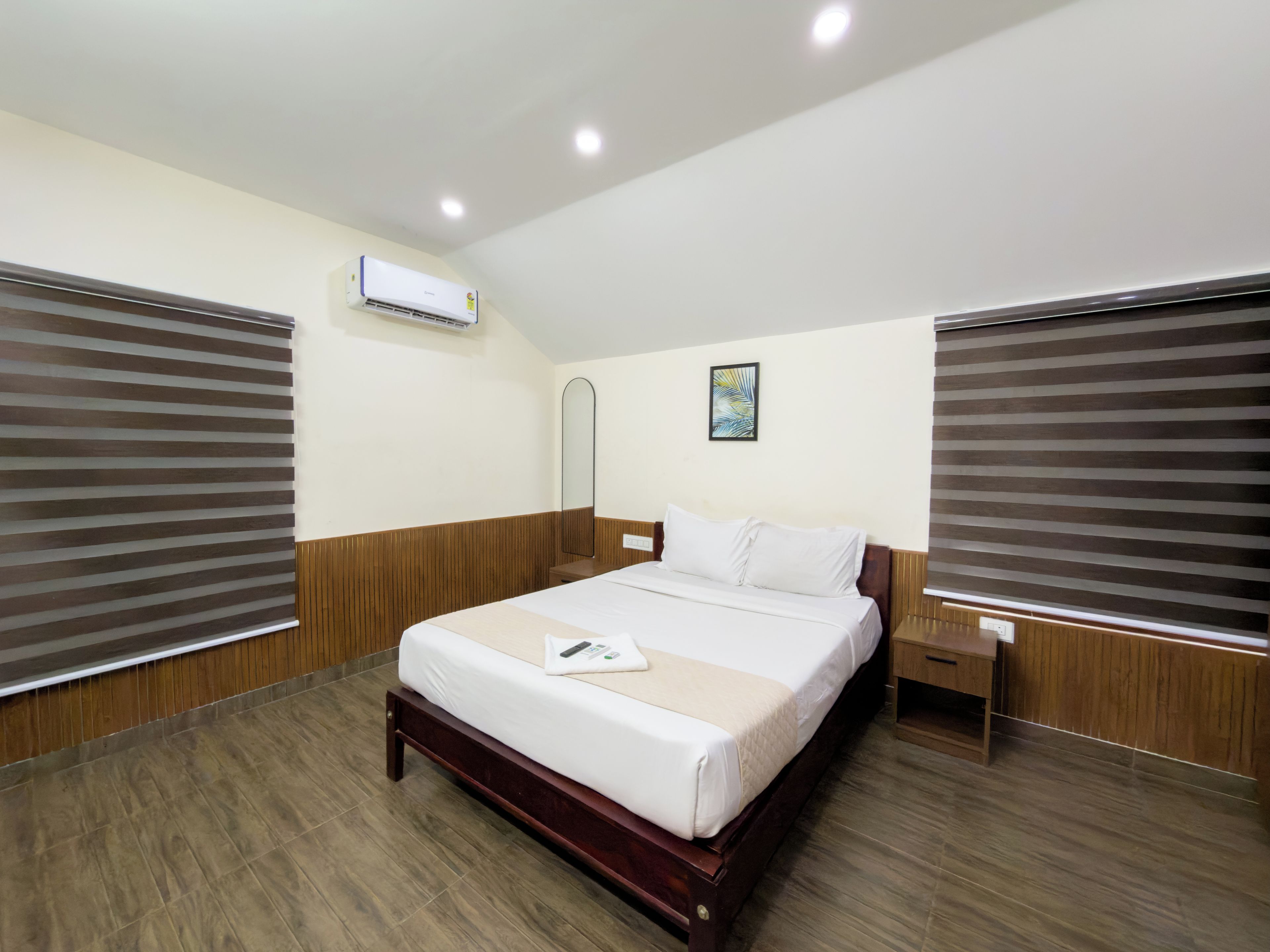 Habitación de hotel con cama de madera, mesita de noche, aire acondicionado y ventana con persianas.