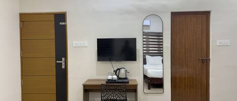 Habitación de hotel con escritorio, silla, televisión y dos puertas.