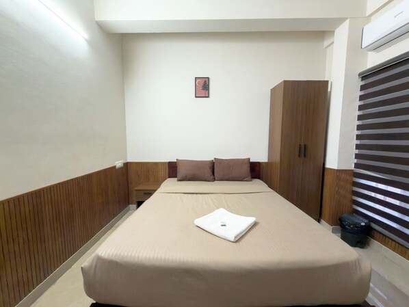 A hotel room with a bed, a nightstand, a wardrobe, and a window with blinds. - CASA GRAND (Aluva)