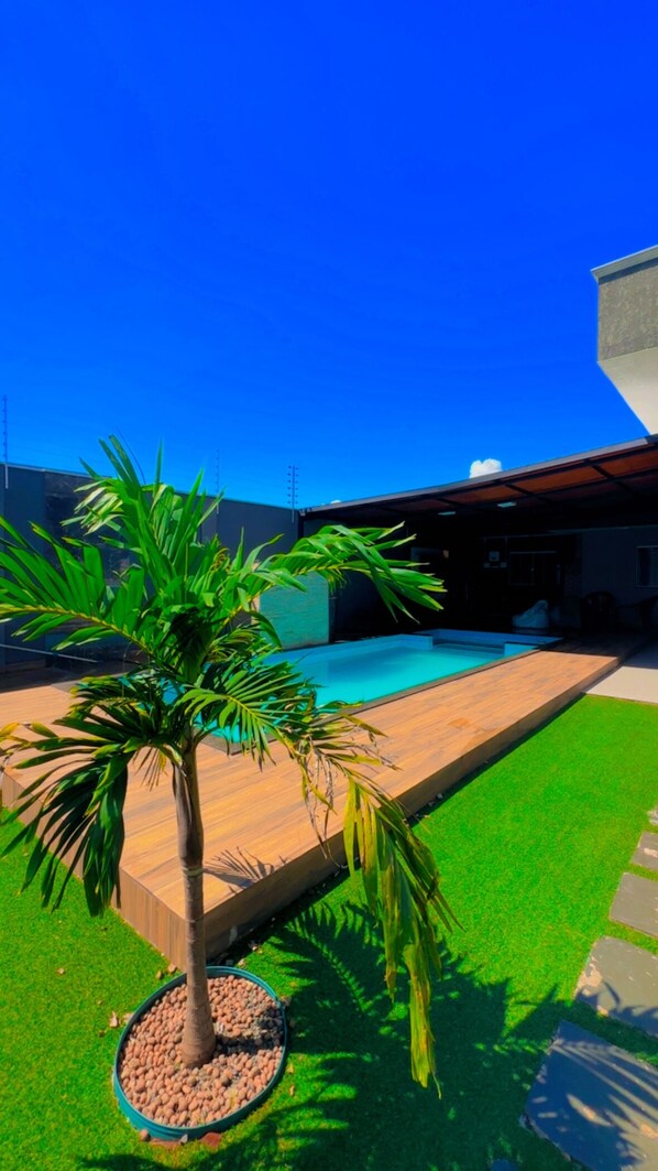 A modern outdoor pool area with a palm tree, artificial grass, and a wooden deck. - Foz do Iguaçu House for the Comfort of your Family (Residencial Cohigaçu Foz do Iguaçu)