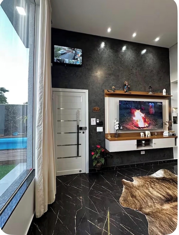 A modern living room with a large flat-screen TV, a cat, a pool view, and a door.