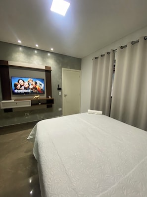 A hotel room with a bed, a TV mounted on the wall, a door, and curtains.
