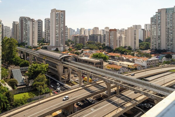 A cityscape with high-rise buildings, a multi-level highway, and a pedestrian overpass. - Studio - Campo Belo with Metro in Front and Rooftop with Sunset. (Brooklin São Paulo)