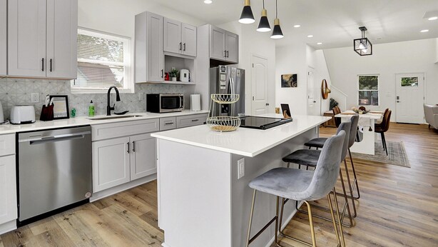 Una cocina moderna con armarios blancos, electrodomésticos de acero inoxidable y una isla central con taburetes de bar.