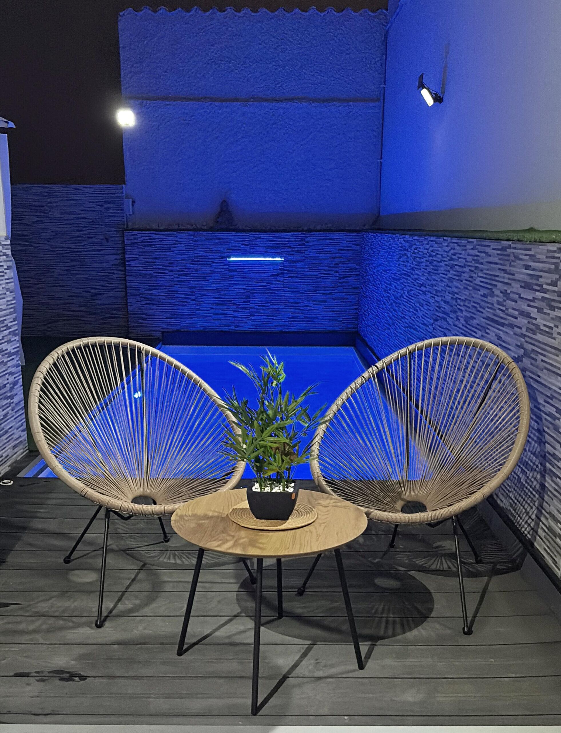 A small outdoor seating area with two wicker chairs and a round table, featuring a potted plant.
