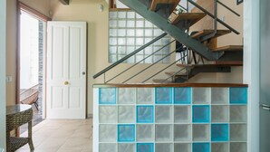 Una escalera con escalones de madera y barandillas de metal, una puerta blanca, un panel de vidrio con detalles azules y una silla de mimbre.