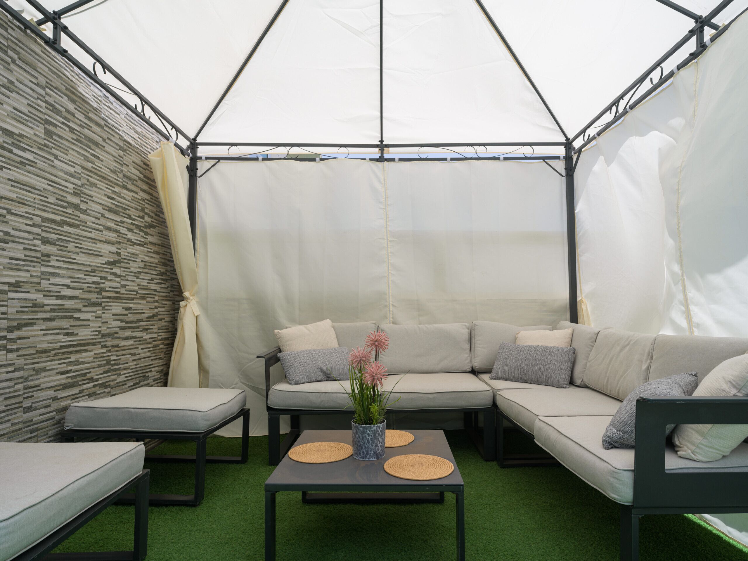 Un espacio al aire libre con carpas, que incluye un sofá modular, dos sillones, una mesita de centro y una planta en maceta.