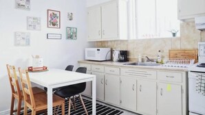 Una kitchenette pequeña con microondas, cafetera y lavabo. Hay una mesa de comedor con sillas y una ventana sobre el lavabo.