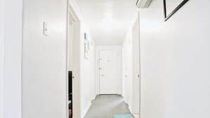 Un pasillo estrecho con paredes blancas y piso gris, que conduce a una puerta al final.