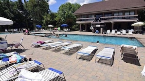 A pool area with lounge chairs and umbrellas, a building with a balcony, and a clear sky.