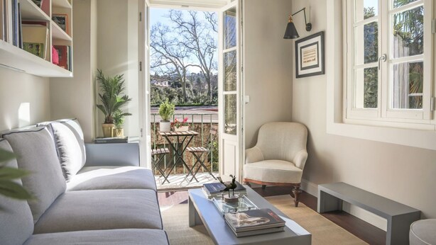 Un salon avec un canapé, une table basse sur laquelle sont posés des livres, un fauteuil et une vue sur un jardin, visible à travers une porte ouverte.