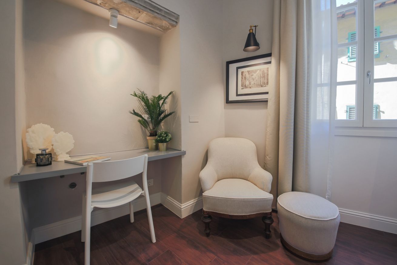 A study with a desk, chair, ottoman, potted plant, and framed artwork.