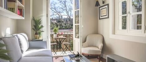 Un salon avec un canapé, une table basse sur laquelle sont posés des livres, un fauteuil et une vue sur un jardin, visible à travers une porte ouverte.